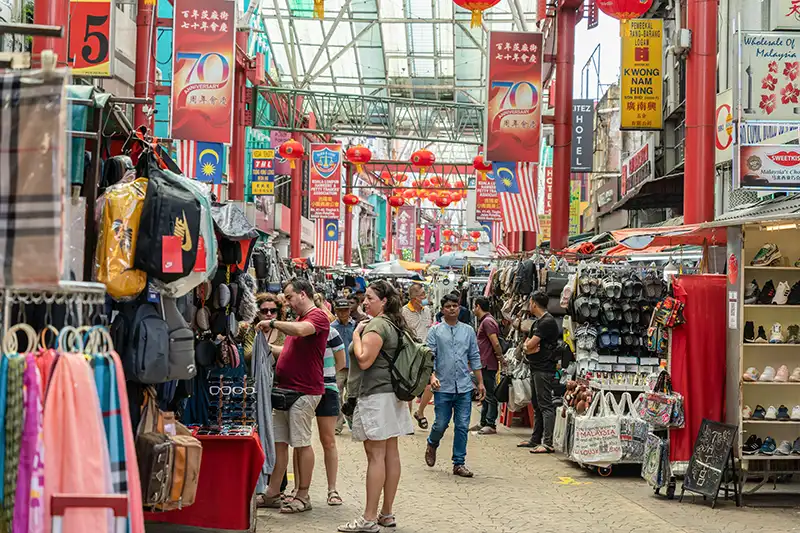 Tourists shopping and bargaining at vibrant Chinatown street market in Kuala Lumpur.
