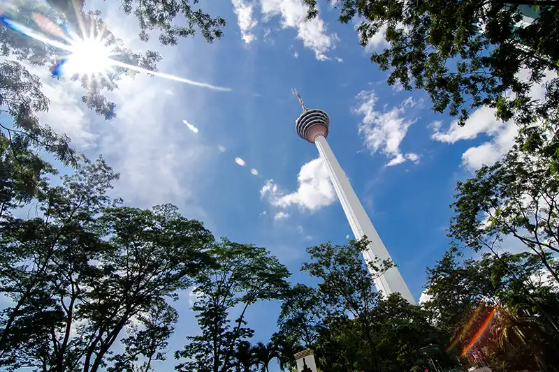 KL Tower viewed from below through trees with a bright sunny sky in Kuala Lumpur.