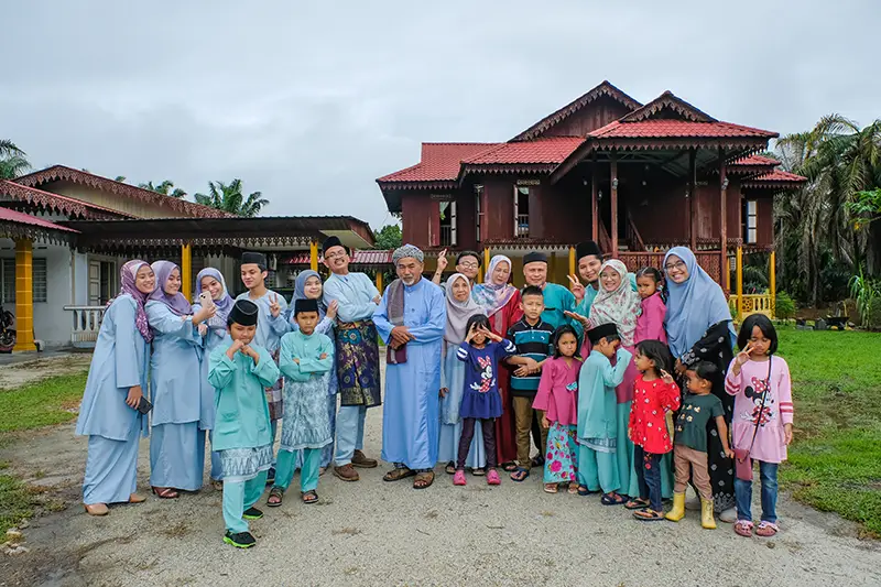 Family gathering during Eid Mubarak festival in Malaysia, standing in front of a traditional Malay house