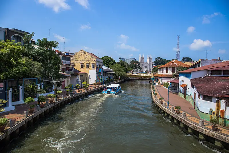 A scenic view of the Malacca River with a river cruise boat and colorful heritage buildings in Melaka, Malaysia.