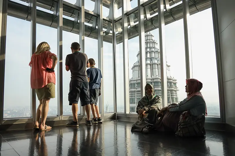 Tourists enjoying the view from the Petronas Twin Towers observation deck, one of the top things to do in KL, with a stunning cityscape backdrop.