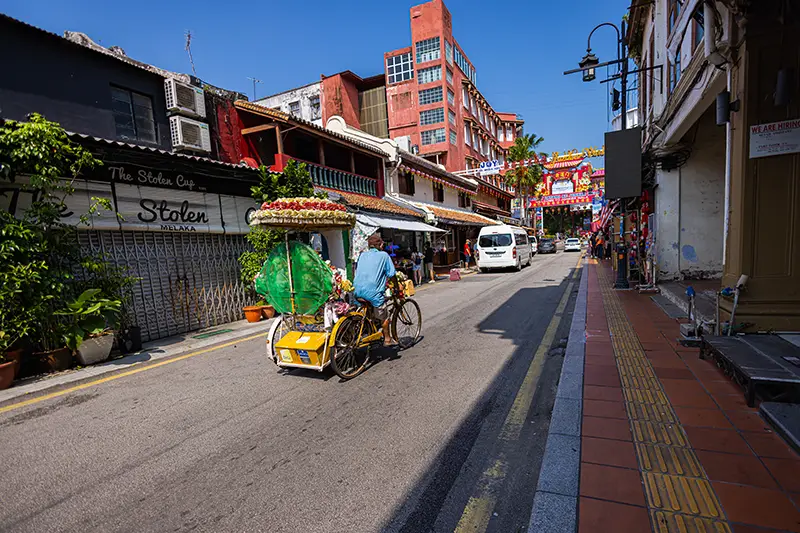 Jonker Street in Malacca during the morning, featuring a colorful trishaw and heritage shophouses along the bustling street.