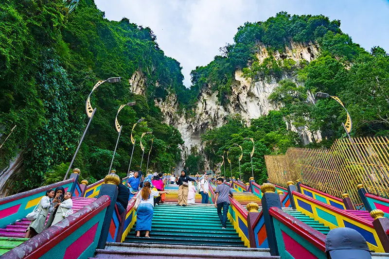 Tourists climbing the colorful rainbow staircase at Batu Caves, a must-visit stop in any Kuala Lumpur itinerary for 2 days