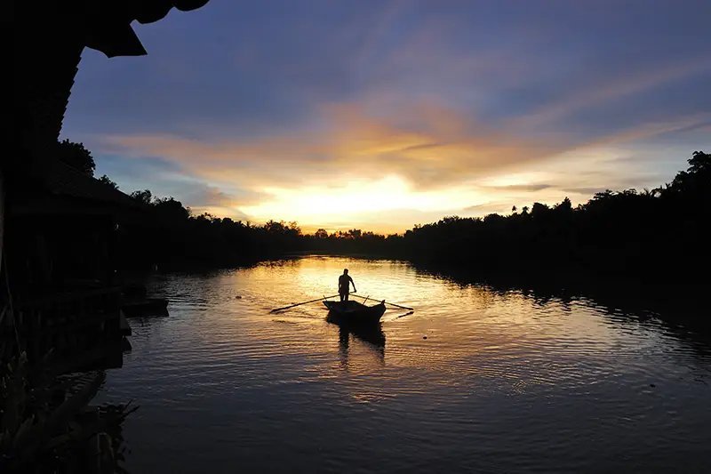 Silhouette of a boatman rowing at sunset in Kuala Selangor Fireflies Park, a peaceful nature experience near Kuala Lumpur