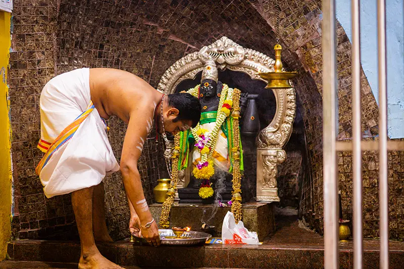 A Hindu priest performing a traditional puja ceremony inside a temple shrine at Batu Caves, one of the unique cultural things to do in Batu Caves